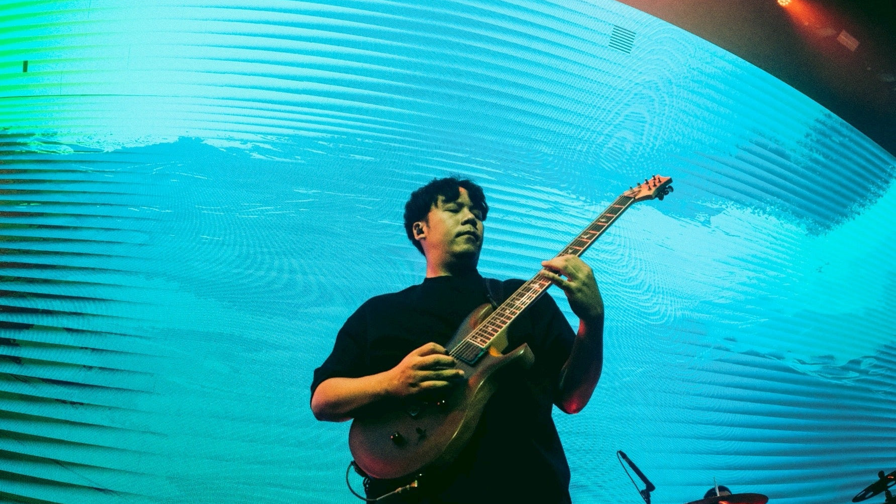 Person playing guitar on stage with a large circular light fixture in the background